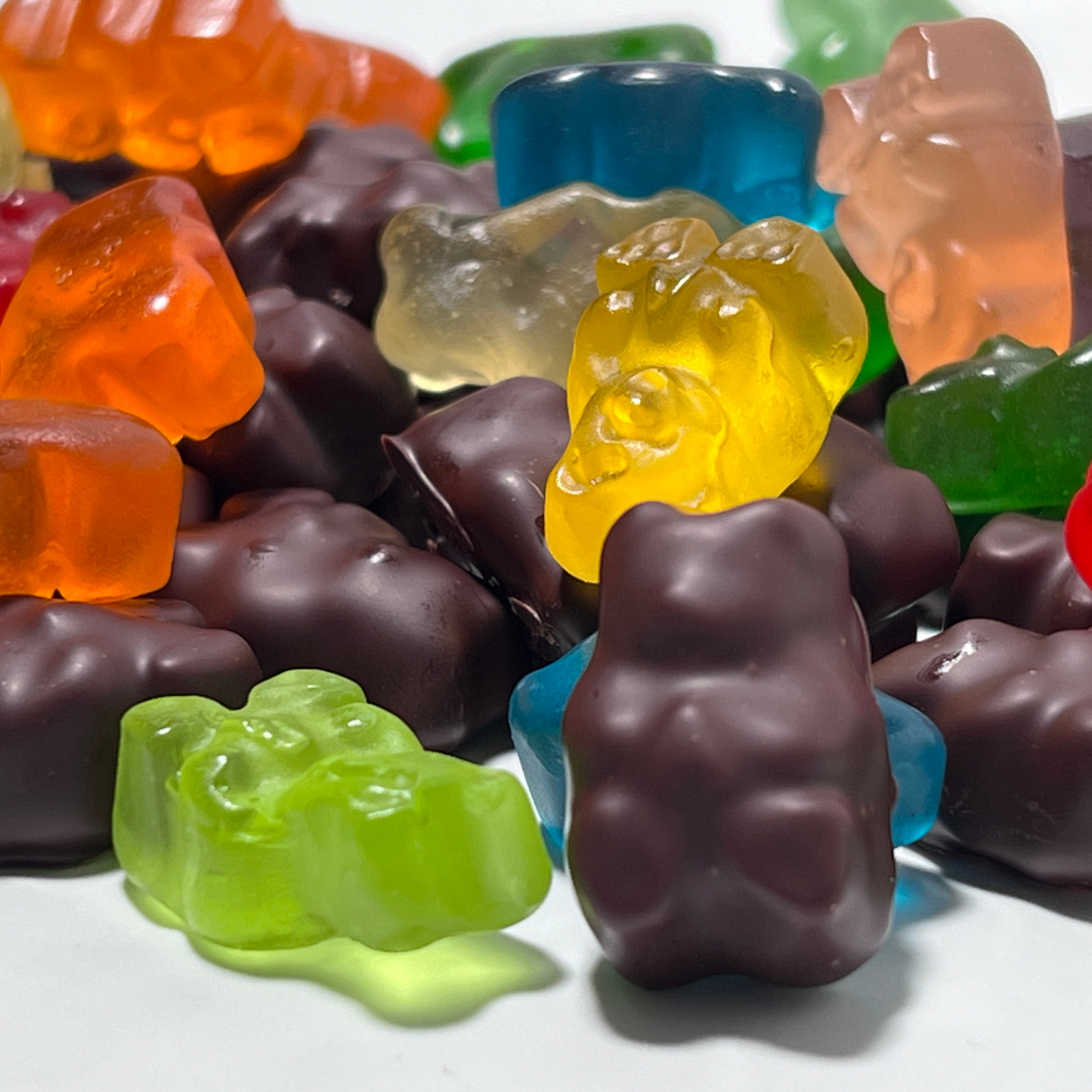A variety of colorful and chocolate-covered Formosa brand gummy bears in a pile together displayed on a white surface.