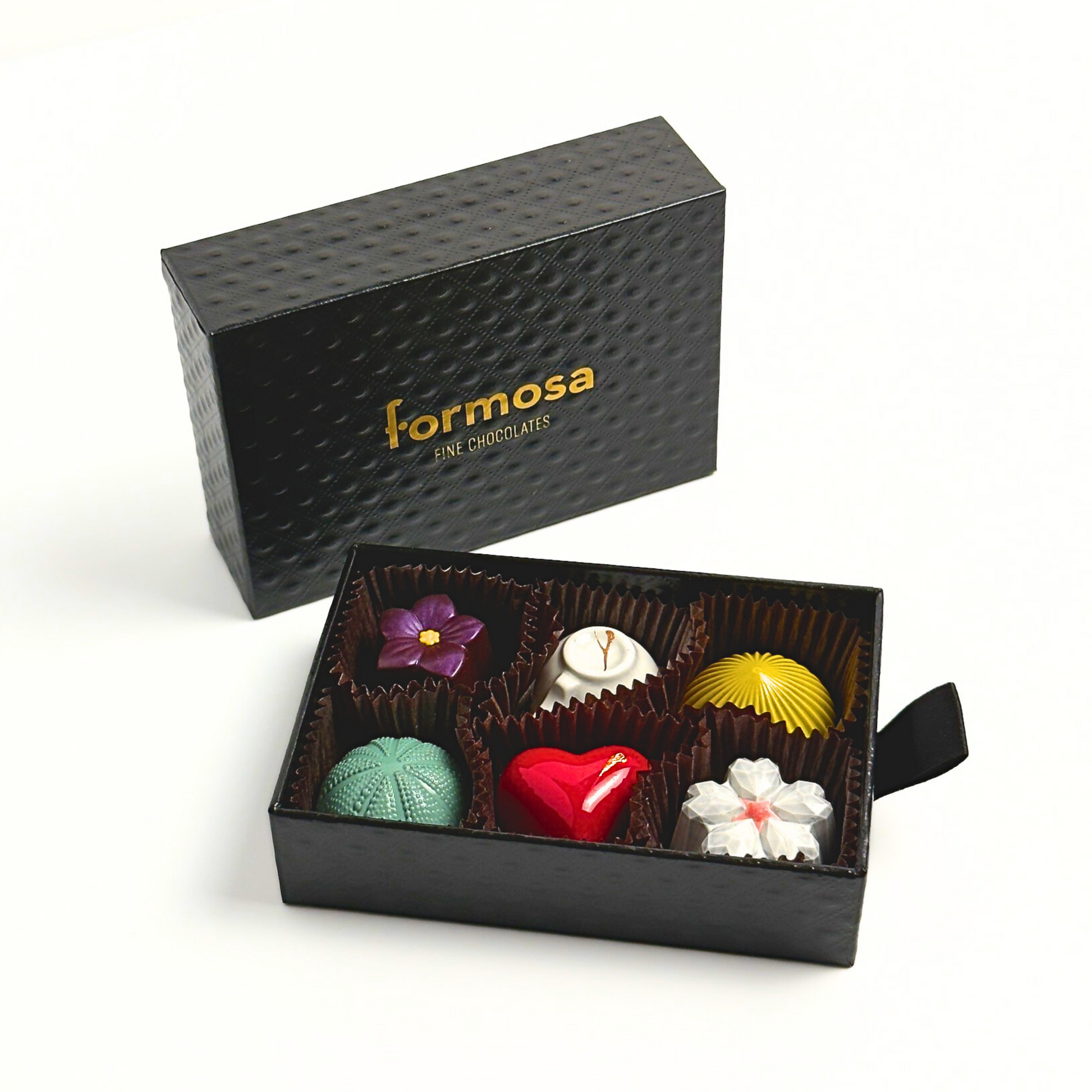 A luxury Formosa brand chocolate box with various colored bonbons neatly arranged in a compartmentalized slot, with the brand name 'Formosa' visible on the exterior in gold color.