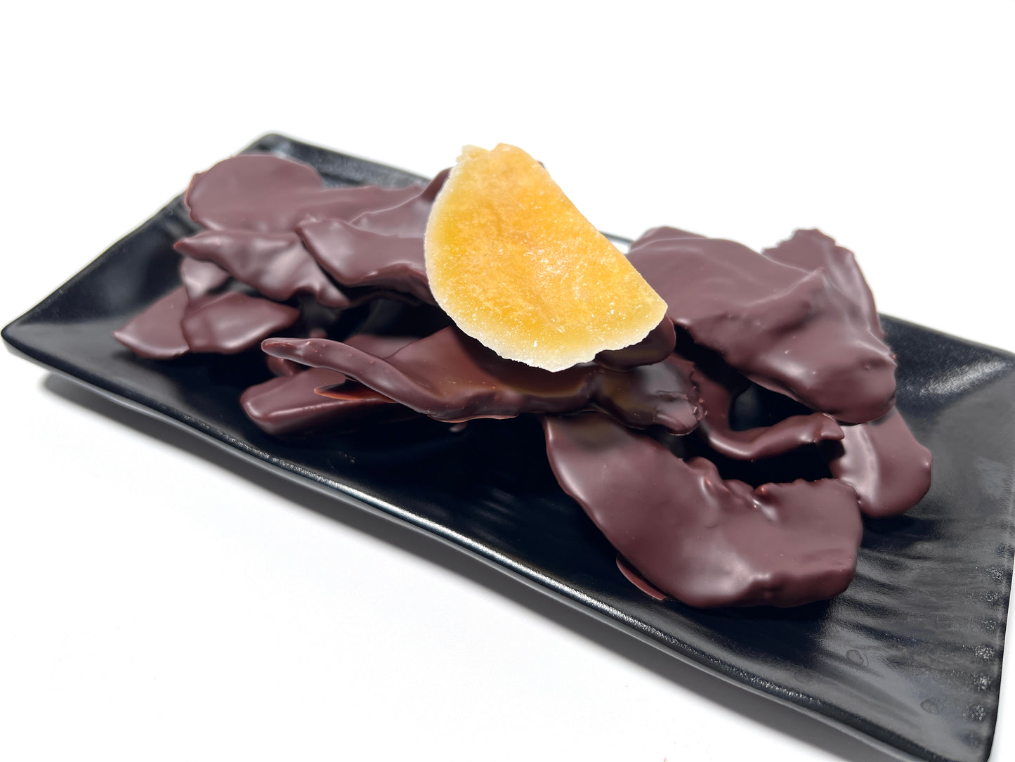 A chocolate-covered dried mango presented on a black plate with additional pieces of chocolate-covered dried mango arranged around it.