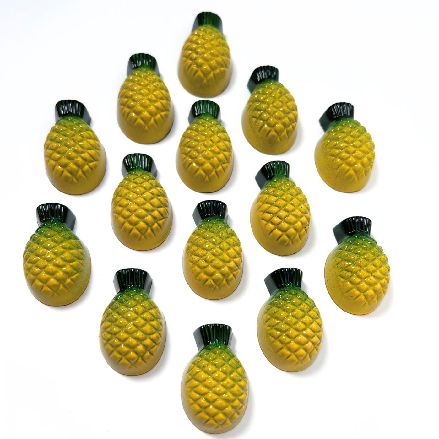 Fourteen Formosa Brand pineapple cake bonbons in the shape of pineapples with embossed pineapple skin texture , colored yellow and green and arranged in a diamond pattern on a white background.