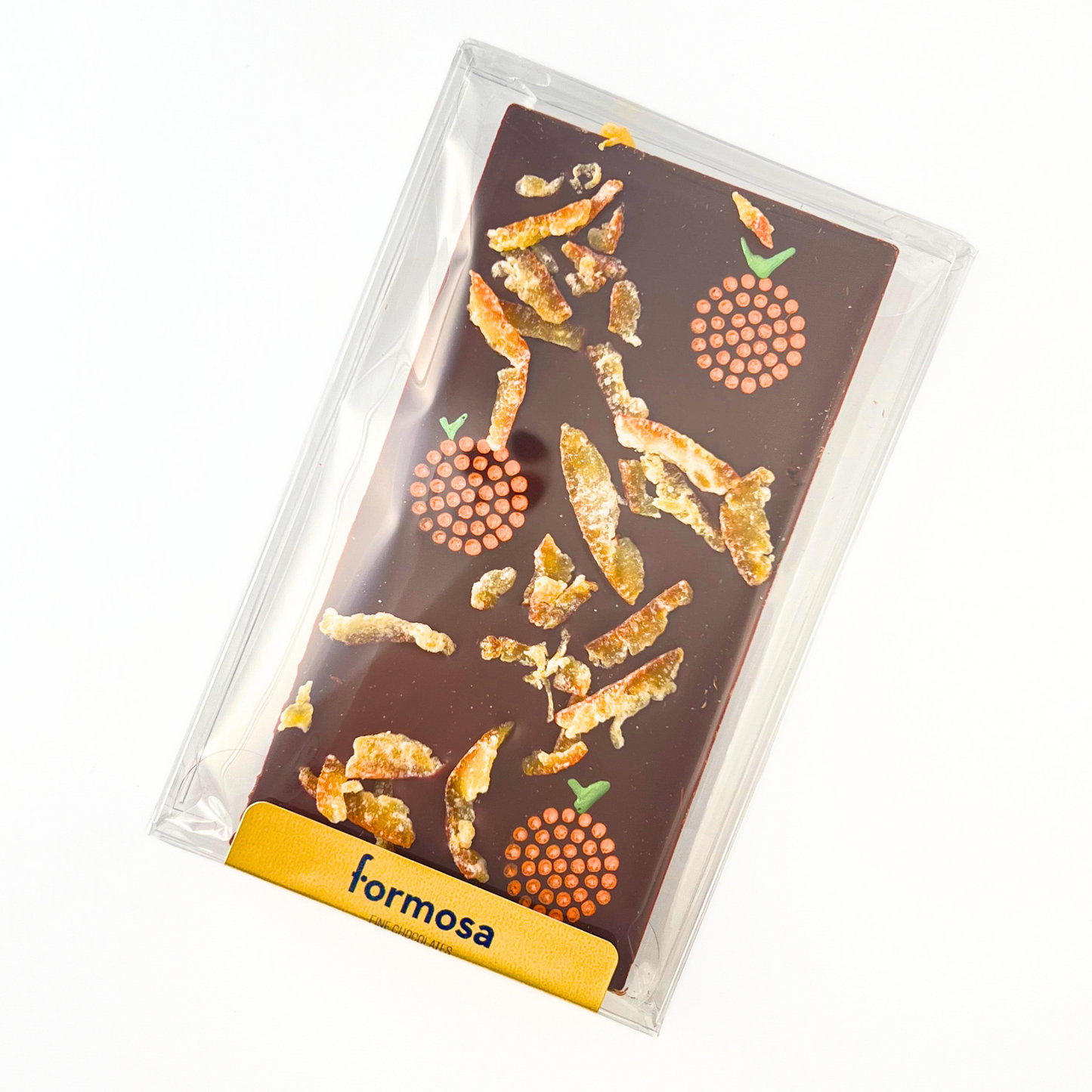 Image of the Iyokan chocolate bar. A dark chocolate bar topped with scattered pieces of Japanese candied Iyokan citrus peel. The bar also features three small, circular stenciled designs that resemble the cross-section of an orange, rendered in tiny orange dots, each topped with a small green stem. The chocolate bar is sealed in food grade clear plastic packaging and rests on a white surface.