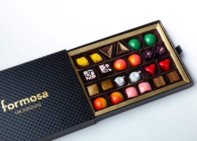 A luxury Formosa brand chocolate box with various colored bonbons neatly arranged in a compartmentalized slot, with the brand name 'Formosa' visible on the exterior in gold color.