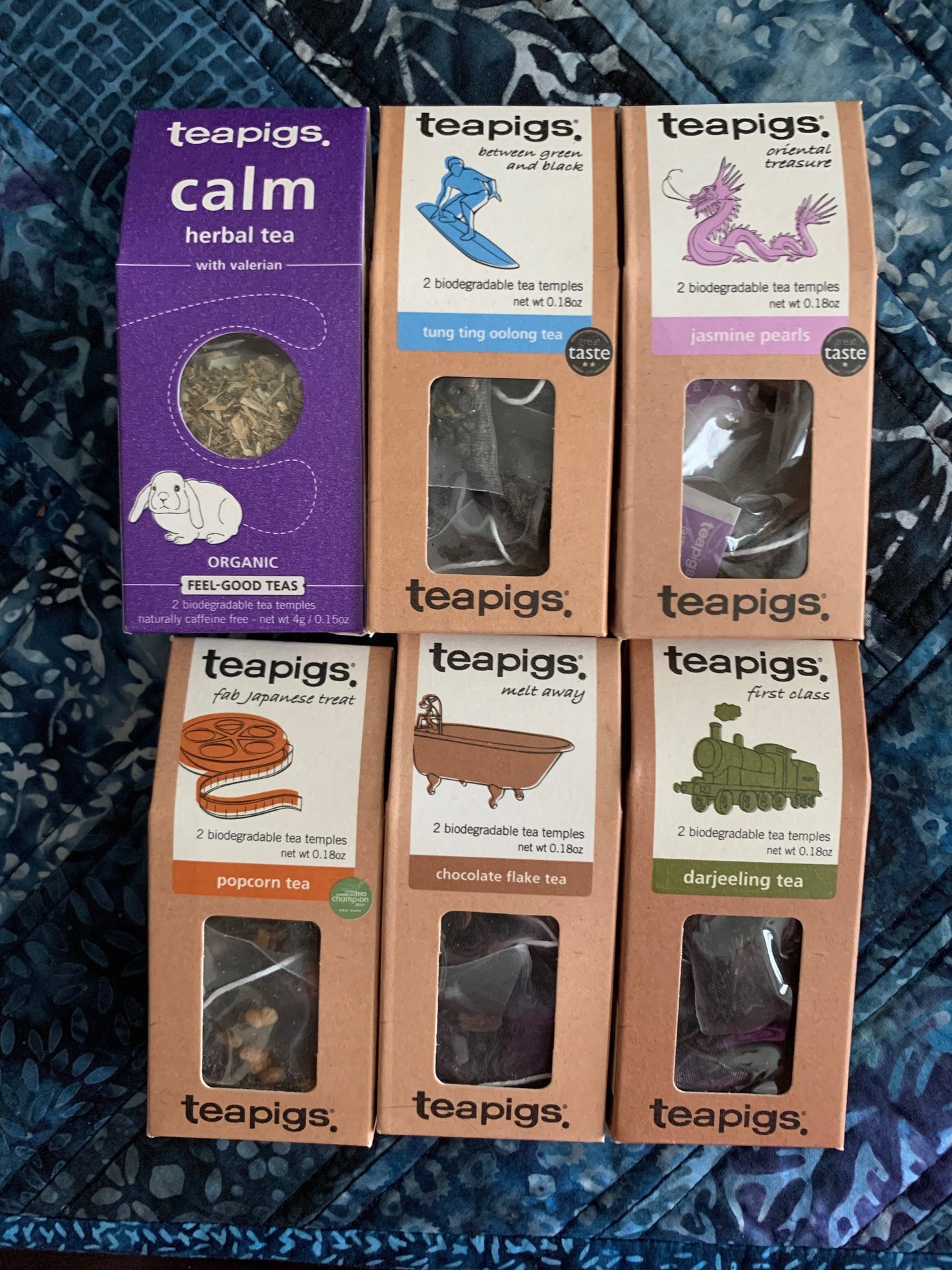 An assortment of packaged teas from the company Teapigs placed on a blue floral pattern fabric.