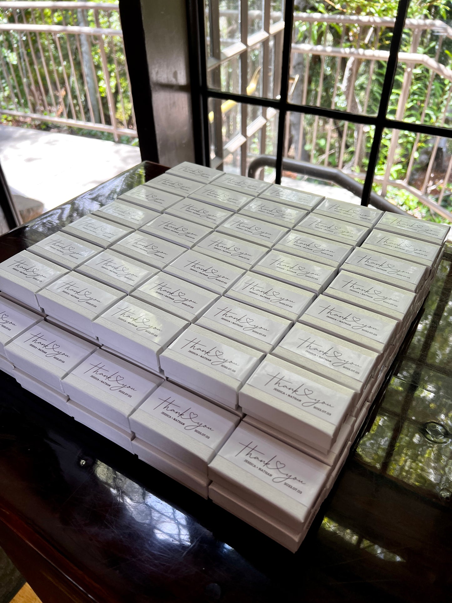 A stack of many white colored customized two piece chocolate boxes with custom label spelling the words "thank you" on top.