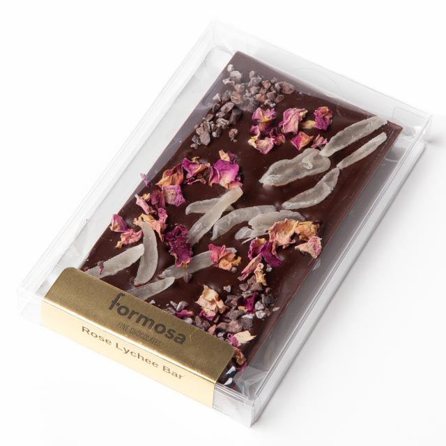 Image of the Rose Lychee bar, a chocolate bar with dried lychee slivers, rose petals, and cacao nibs on top visible through the clear plastic packaging.
